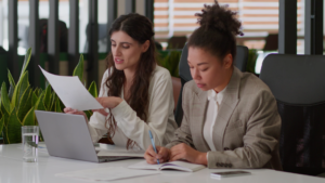 two women with paper and laptop doing corporate work